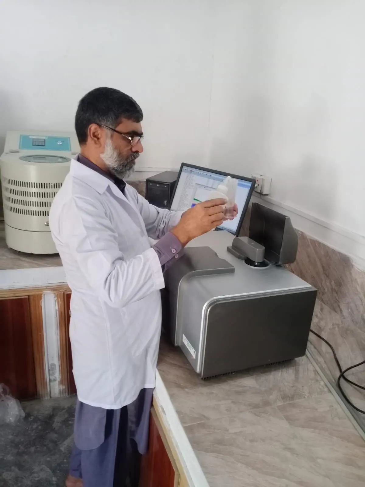 A laboratory technician in a white coat operating an analyser at a bench