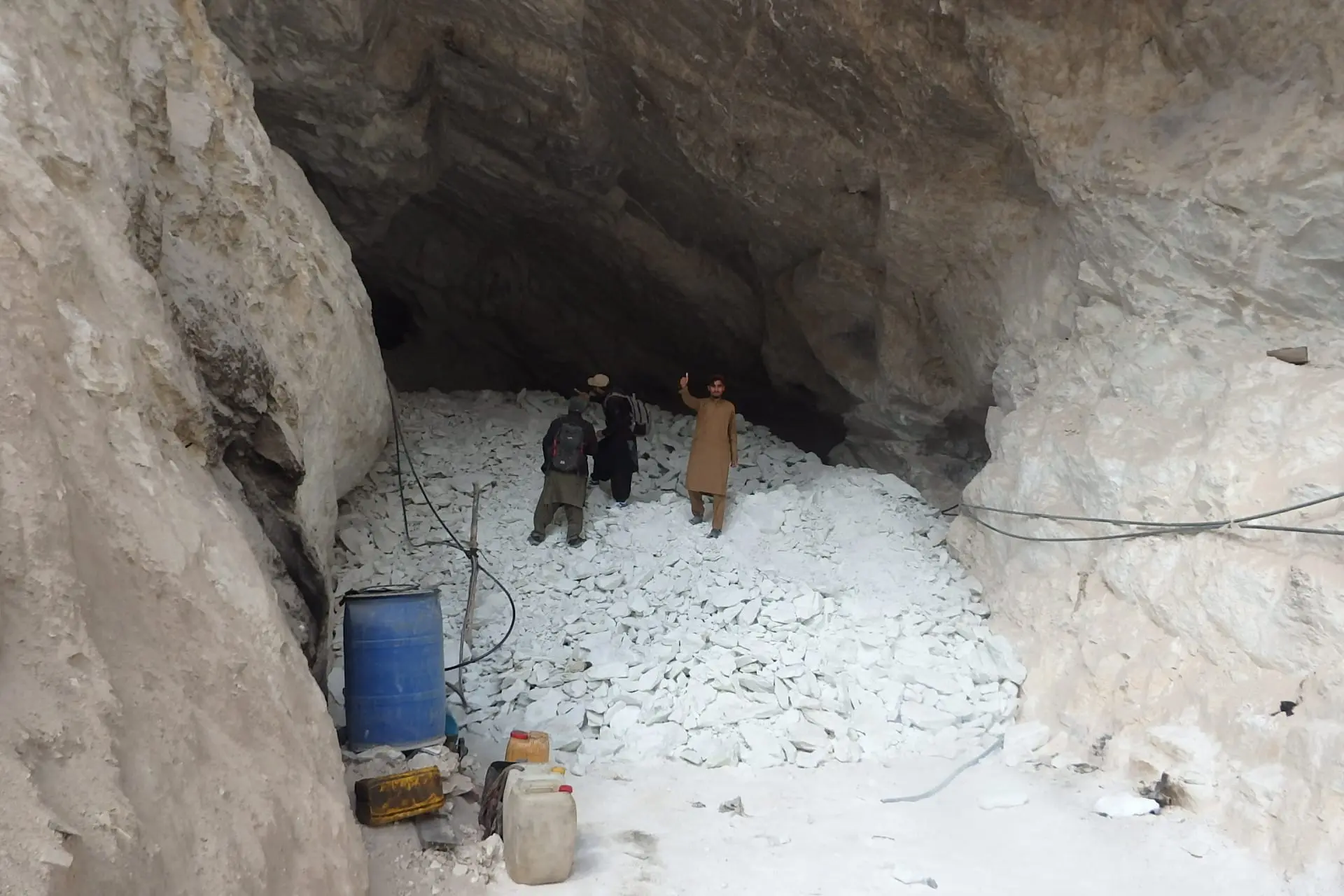 Workers in a large rock cavity beside a pile of broken white rock